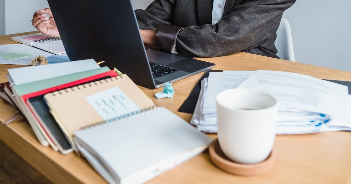 Escritorio de un estudio contable con una notebook abierta, cuadernos, carpetas con papeles y una taza