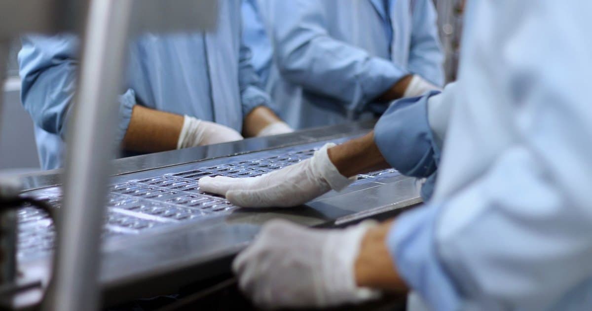 Operarios de laboratorio con ambo y guantes trabajando en una línea de envasado de comprimidos